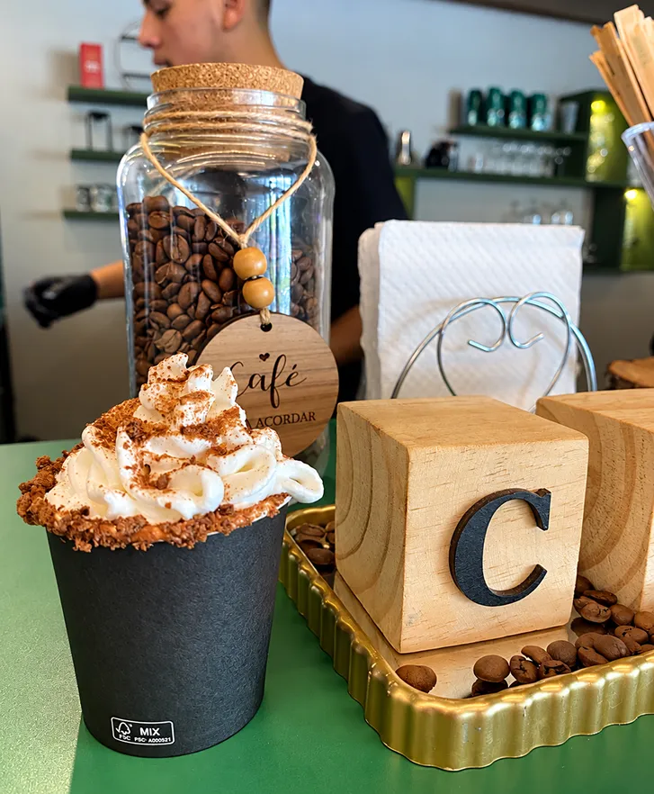 Café especial com chantilly e canela servido em copo, ao lado de pote de grãos de café