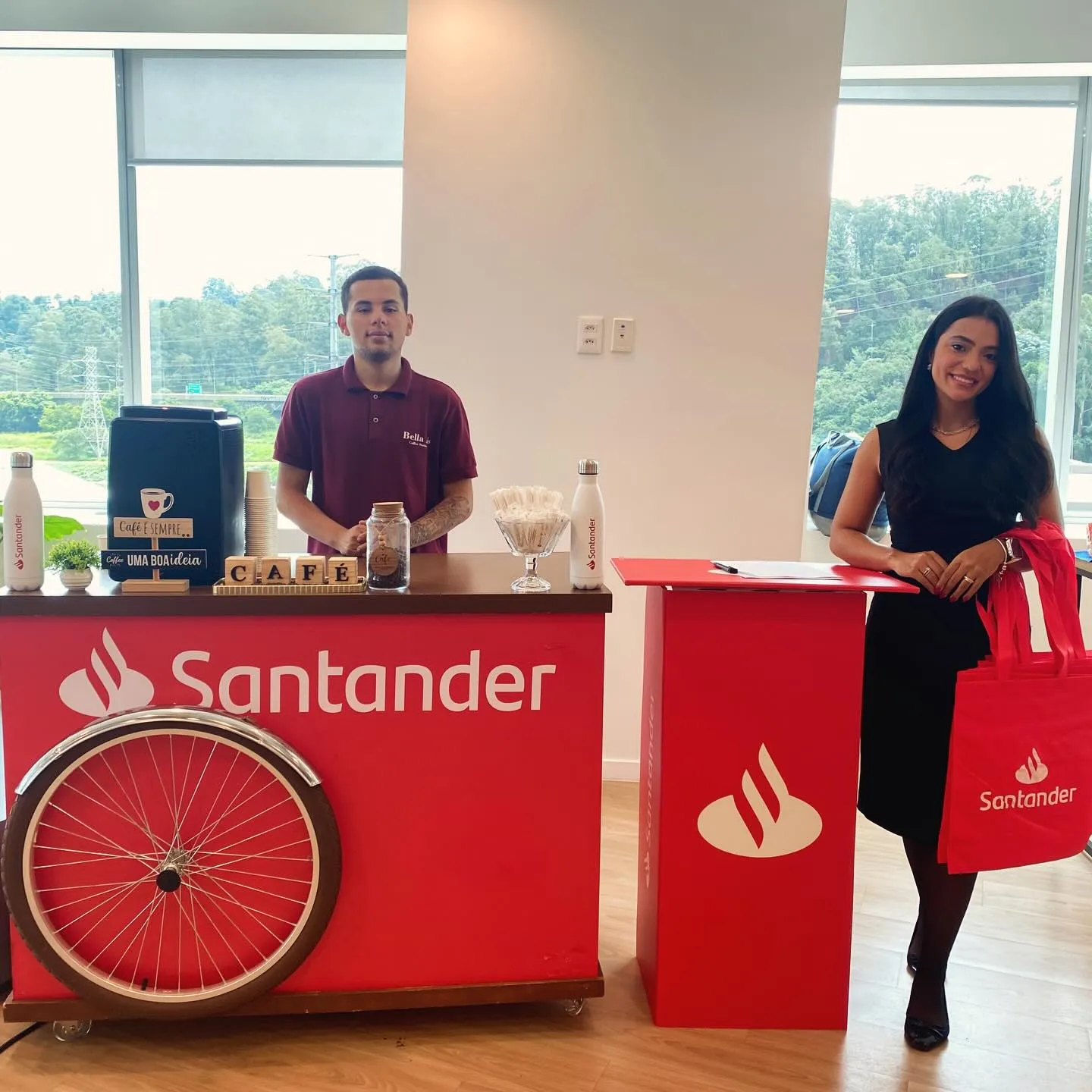 Carrinho de café com a identidade visual do Santander em evento corporativo, com barista e anfitriã