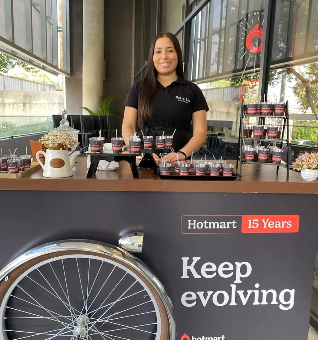 Barista da Bella Lis em carrinho personalizado Hotmart 15 Years com copos da marca